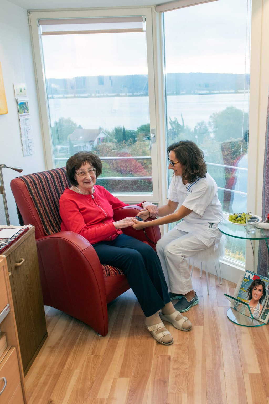 Une aide-soignante et une résidente sont assises sur des chaises dans la chambre de la résidente.